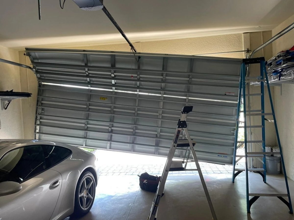 Partly open garage door above a silver car, with two ladders in the work area